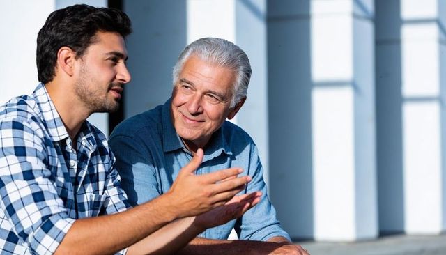 Young man and older man chatting on sunlit urban steps, warm intergenerational connection