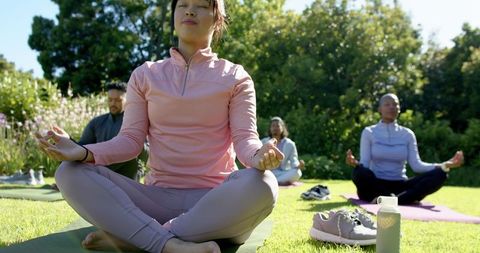 Outdoor guided group meditation and mindfulness practice on sunny lawn for wellness yoga