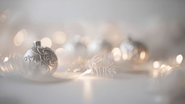 Elegant silver christmas bauble with glitter swirl, white pine sprig and warm bokeh lights