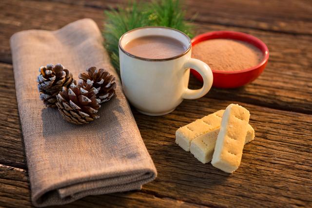Pine cone, coffee cup, coffee powder, sweet food, and christmas fir with napkin on wooden plank