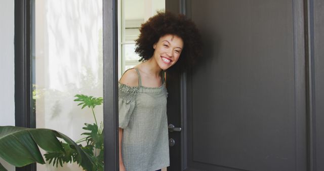 Portrait of smiling biracial woman standing at open front door and welcoming guest. Home and lifestyle.