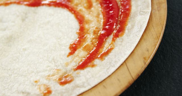 This close-up photo of an uncooked tortilla spread with tomato sauce is ideal for food blogs, cooking tutorials, or online menus. It also works well for marketing content about Italian cuisine, kitchen appliances, or recipe development.
