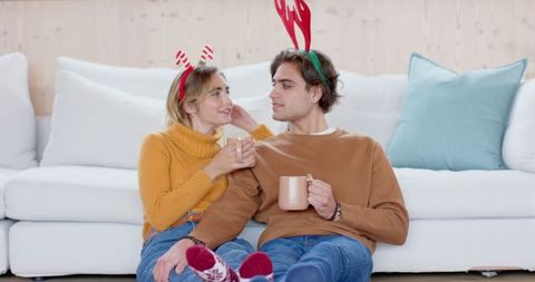 Happy couple relaxing with hot drinks wearing festive antlers