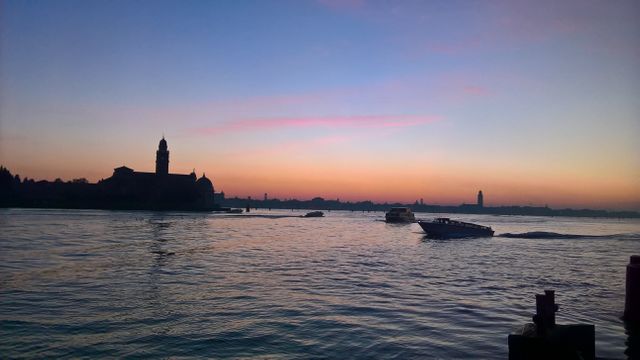 Iconic Venetian water scene at sunrise showing boats on calm water with a silhouette skyline in the background. Shaded structures enhance serene and picturesque ambiance, perfect for travel blogs, tourism advertisements, or European travel brochures.