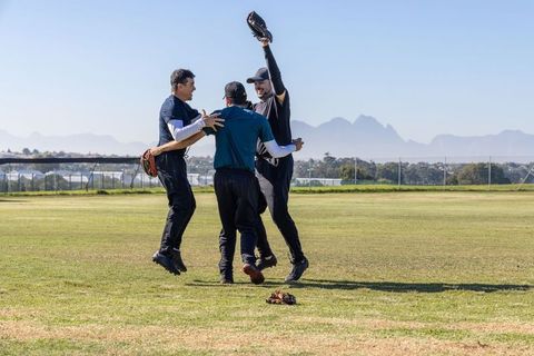 Baseball teammates celebrating jumping catch in outfield with sunlit mountain backdrop