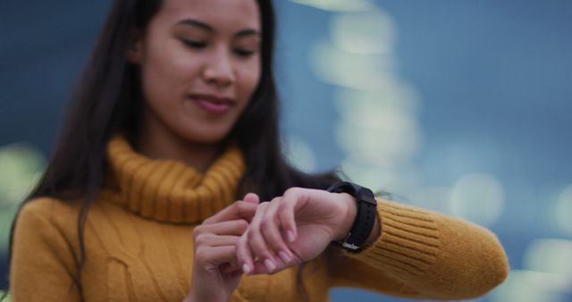 Image offers a focused view of a woman checking time on smartwatch in modern urban environment. Suitable for promoting wearable technology, lifestyle blogs, time management tips, and modern urban living themes.
