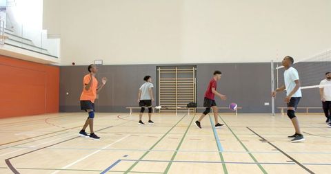 Diverse male volleyball players practicing on indoor gym court wearing knee pads