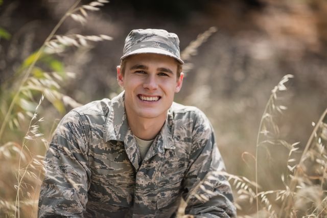 Portrait of happy military soldier crouching in grass in boot camp