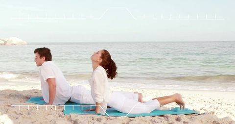 Couple practicing partner yoga backbend on sandy beach with turquoise mats