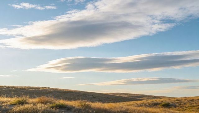 Rolling golden prairie hills glowing under lenticular clouds in soft low sunlight panorama