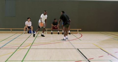 Men dribbling under pressure on indoor basketball court with teammates watching