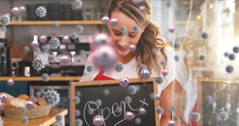 Smiling Barista Holding Open Sign in Café with Floating Virus Particles