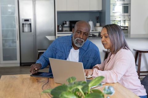 Mature couple working together on laptop at modern kitchen table planning finances