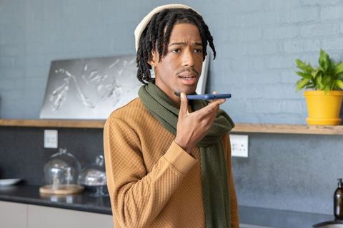 Young African American man speaking into smartphone while standing in modern kitchen