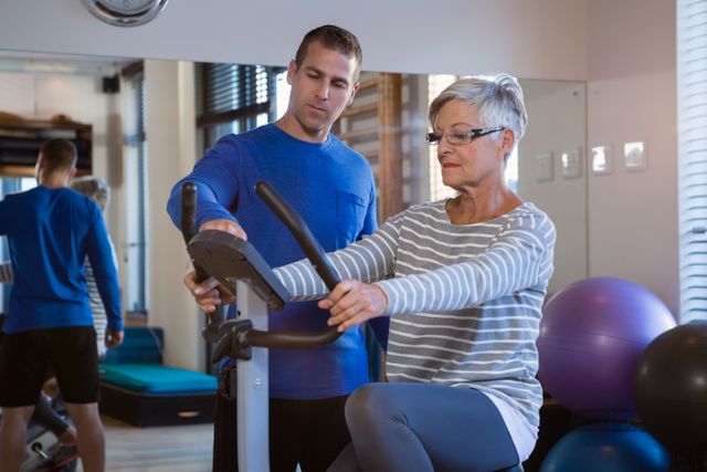 Senior woman training with a physiotherapist on an exercise bike in a clinic. Useful for illustrating physical therapy, elderly fitness, rehabilitation exercises, healthcare services, and the importance of guided training for seniors.