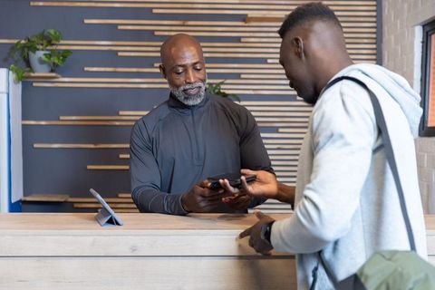 African american receptionist and guest exchanging phones at clean modern wooden front desk