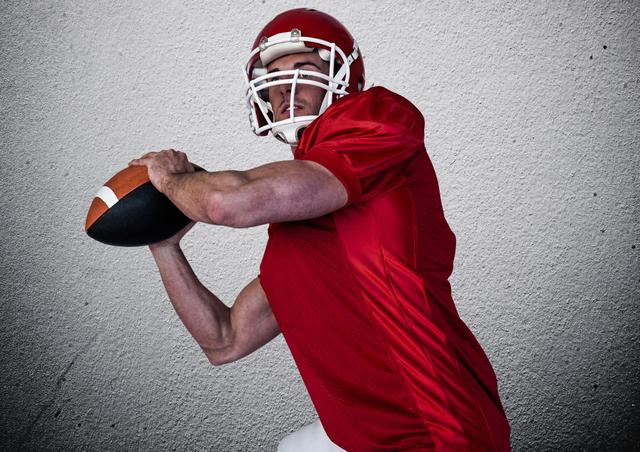 American football player in red uniform holding ball, against a white wall background. Ideal for sports-related articles, athlete training programs, team-building events, motivational posters, and fitness industry promotions.