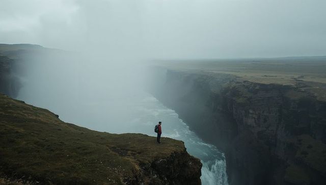 Hiker standing on cliff edge above misty canyon waterfall surveying vast remote plateau