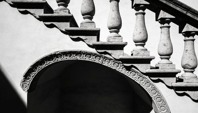 Ornate stone balustrade and carved arch casting dramatic shadows in historic courtyard