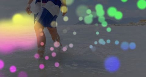 Person walking through shallow coastal waters with colorful bokeh effect