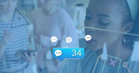 Black businesswoman writing on glass board during team brainstorming with chat alert
