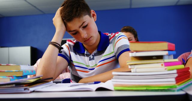 Teenage boy sitting in classroom, surrounded by a stack of books and looking stressed. Ideal for educational articles, blogs on academic stress, mental health resources for students, back-to-school promotions, and content related to study habits.