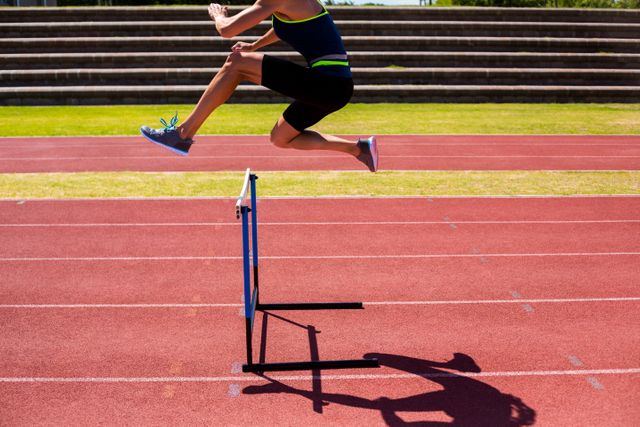Female athlete jumping over a hurdle on a track during a race. Ideal for use in sports-related content, fitness and training programs, athletic event promotions, and motivational materials.