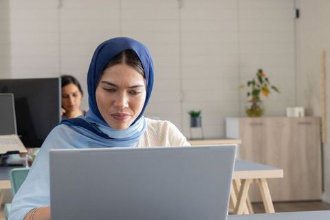 Muslim woman working on laptop in minimalist coworking office with colleague and plants