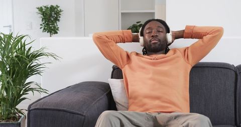 Calm African American man relaxing with headphones on modern gray sofa at home