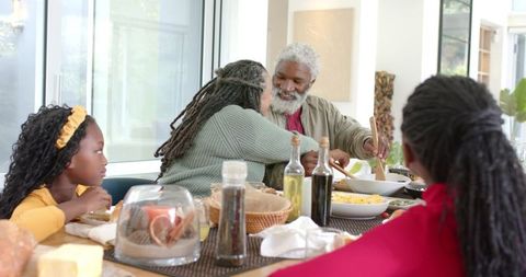 Multigenerational Black Family Sharing Joyful Sunlit Dinner While Grandfather Serves