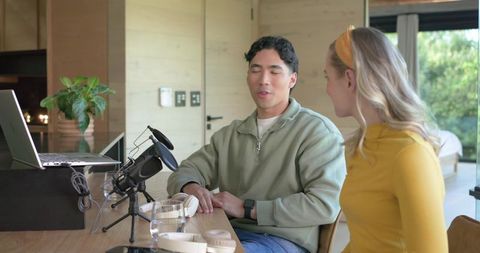 Couple recording home podcast conversation with microphone and laptop for casual interview
