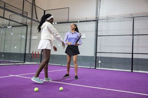 Female players practicing padel on vibrant purple court during friendly coaching session