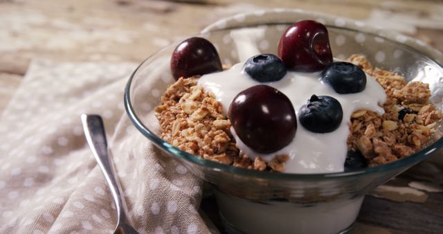 A bowl of granola topped with yogurt and fresh berries sits on a wooden surface, with copy space. Ideal for a healthy breakfast or snack, the image emphasizes nutritious eating.