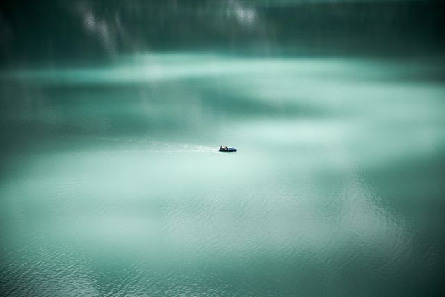 Boat is slowly moving on calm turquoise lake, creating a serene and peaceful scene. This image is perfect for promoting outdoor activities, nature travels, and relaxation retreats. Suitable for use in travel blogs, magazines, and websites focused on nature, leisure, or mindfulness.