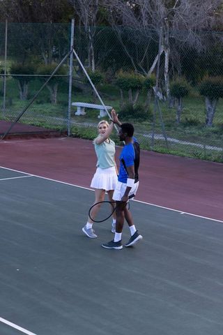 Mixed-race tennis partners celebrating high-five on outdoor court after point