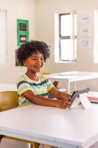 Smiling african american boy using tablet at classroom desk for learning and technology