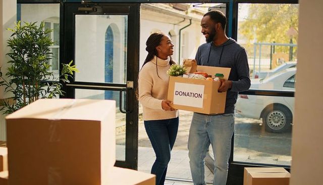 Smiling couple carrying donation box into community center, volunteering together