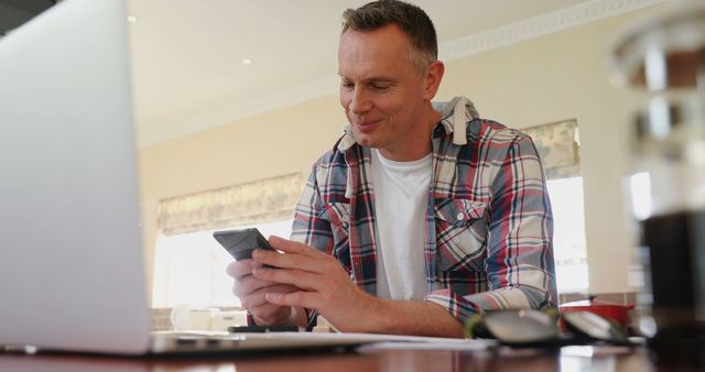 Man in Casual Shirt Checking Phone While Working on Laptop - Download Free Stock Images Pikwizard.com