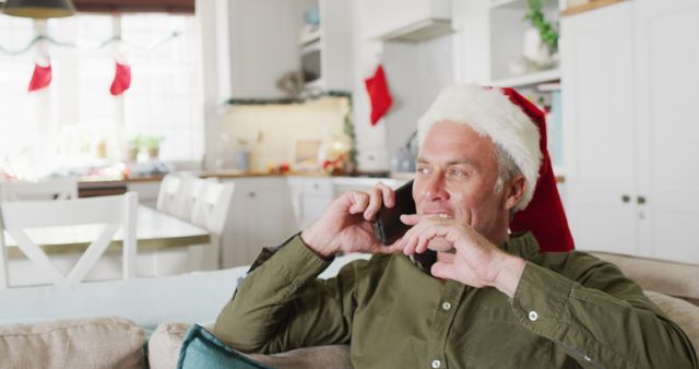 Middle-aged Man in Santa Hat Talking on Phone in Festively Decorated Kitchen - Download Free Stock Images Pikwizard.com