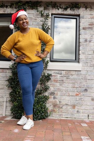 African american woman smiling in santa hat and mustard sweater on brick patio festive holiday