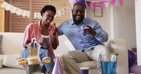 African American couple laughing on couch at home birthday celebration with cupcakes