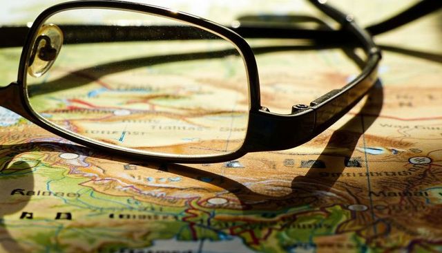 Rectangular eyeglasses resting on vintage map, magnifying topography and casting shadows