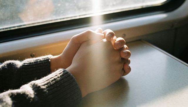 Clasped hands resting on train table in warm sunbeam, quiet travel intimacy