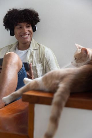 Man Relaxing with Headphones and Tablet Near Cat at Home