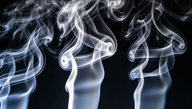 Rising spiral smoke plumes forming translucent ribbon curls against black backdrop