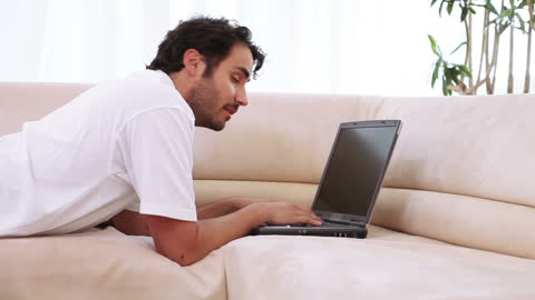 Young Man Working on Laptop While Relaxing on Couch