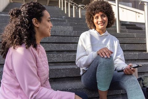 Multicultural friends chatting on outdoor steps in casual activewear holding smartphone