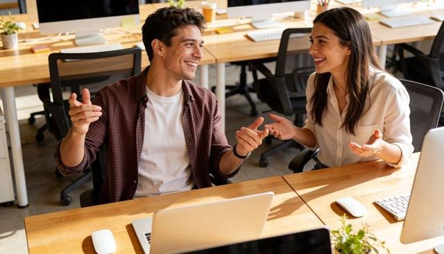 Coworkers collaborating and smiling at open-plan desk with laptops and plants