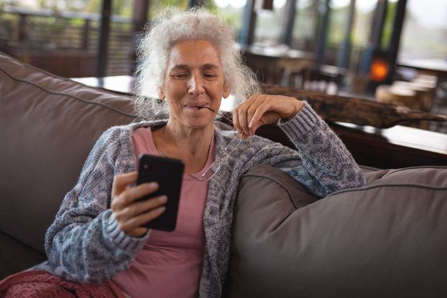 Smiling caucasian senior woman sitting on sofa and using smartphone - Download Free Stock Photos Pikwizard.com