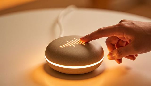 Hand touching pebble smart speaker with amber waveform touch light for cozy home